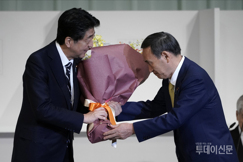 아베 신조(왼쪽)가 지난 14일 도쿄 한 호텔에서 열린 자민당 총재 선거에서 당선된 스가 요시히데에게 꽃다발을 건데며 축하하고 있다 ⓒ뉴시스