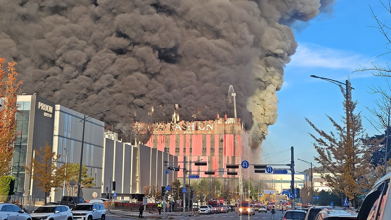 15일 오전 6시께 충남 천안시 동남구 풍세면 용정리에 위치한 이랜드패션물류센터 상층부에서 화재가 발생해 검은 연기가 건물을 뒤덮은 가운데, 소방대원들이 불을 끄기 위해 소방호스로 물을 뿌리고 있다. [사진=뉴시스]